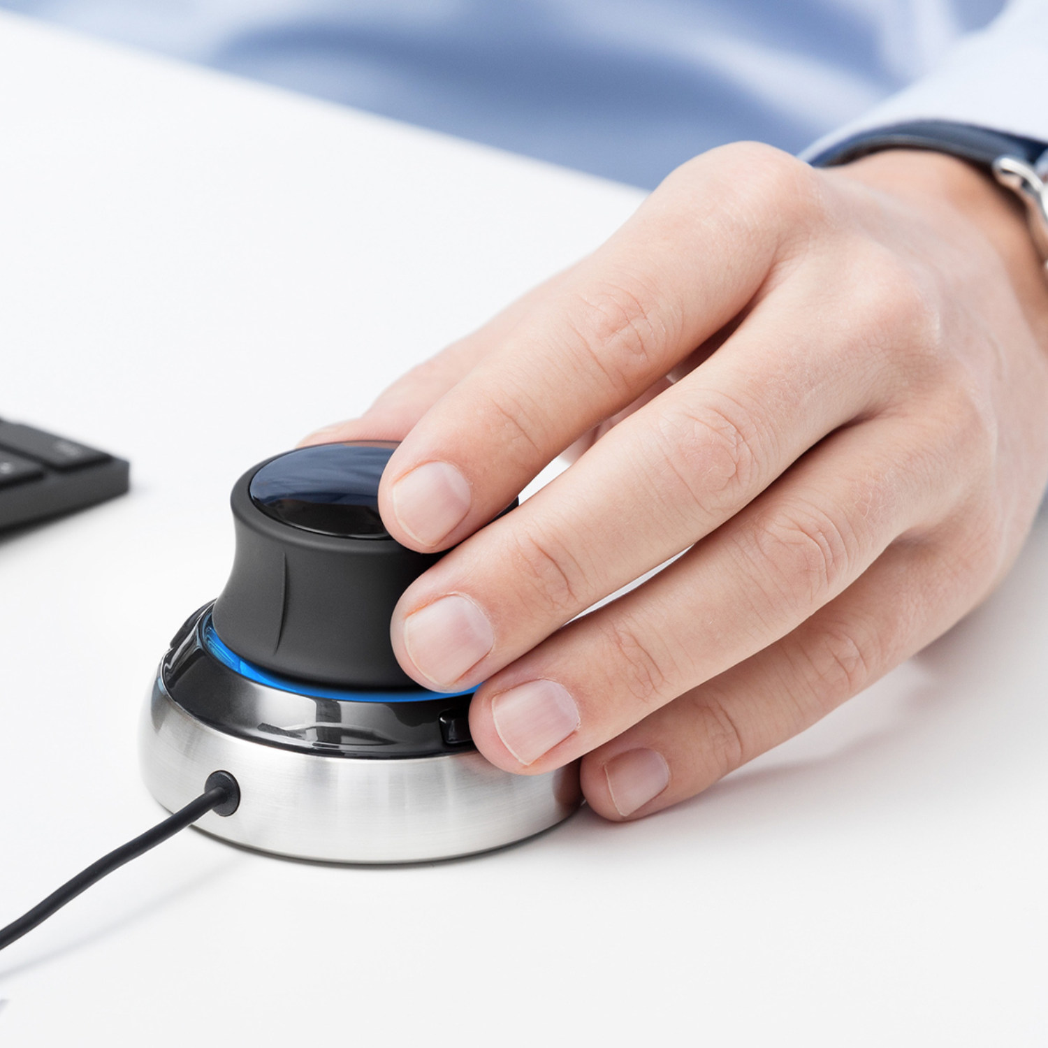 Hand operating the 3Dconnexion SpaceMouse® Compact, highlighting the ergonomic design and smooth control knob with a brushed metal base on a clean, minimal desk setup.